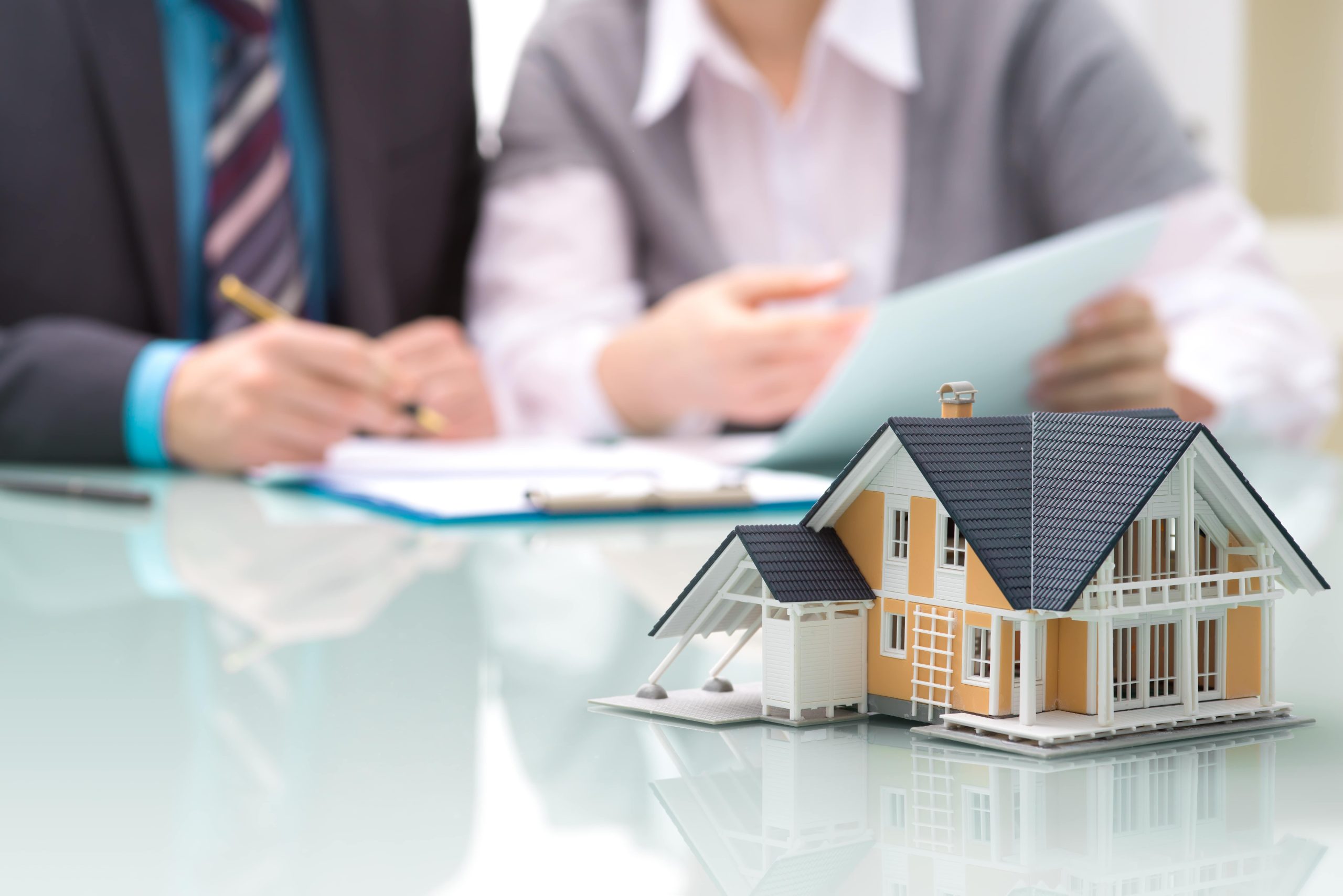 House model in focus, in background lenders reviewing paperwork
